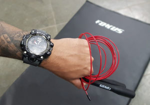 Imagem em destaque de mão masculina com relógio e corda de pular a frente de um tapete de exercícios fokus