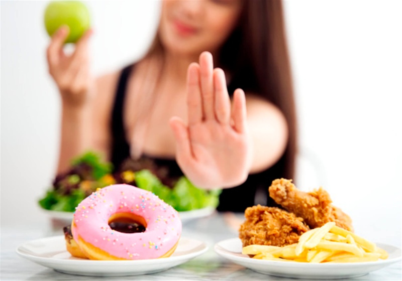 Imagem de uma mulher rejeitando frituras e doces e comendo salada 