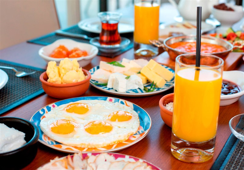 Imagem de uma mesa de café da manhã com ovos, suco, queijos e frutas