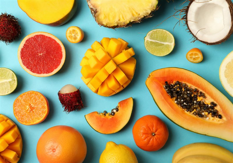 Imagem de uma mesa azul com frutas como mamão, laranja, limão e manga