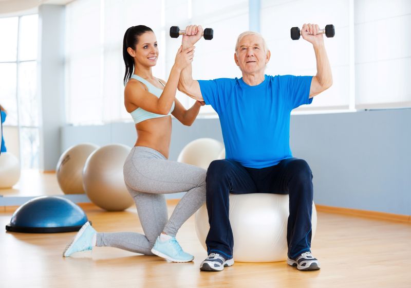 Imagem de um homem idoso fazendo exercícios com ajuda de uma profissional